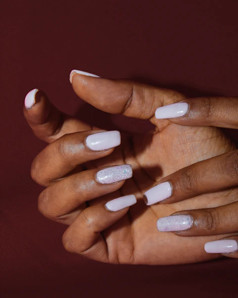Manos con uñas acrílicas largas en blanco lechoso sobre fondo vino