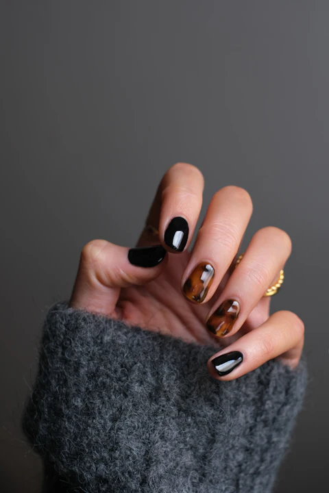 Uñas con efecto carey y negro brillante junto a un anillo dorado