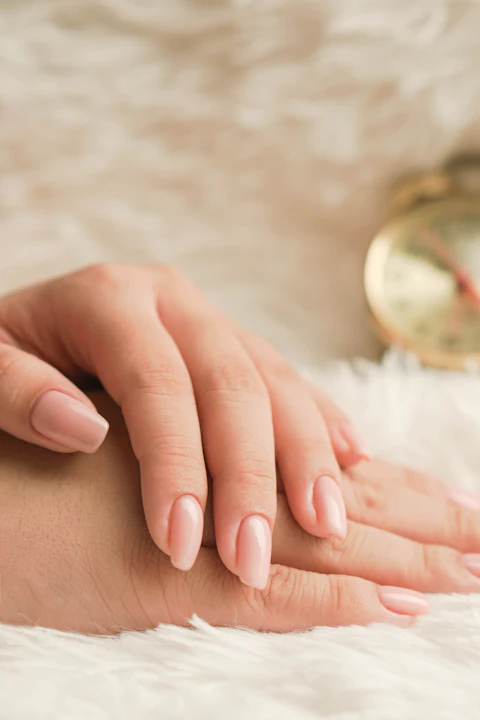 Manos con uñas nude cortas sobre una manta blanca
