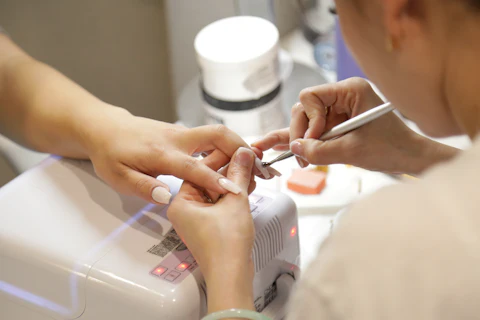 Manicurista aplicando esmalte a una clienta en la mesa de trabajo