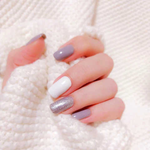 Uñas en gel en tonos malva, blanco y glitter plateado sobre un suéter blanco