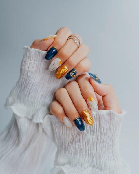 Nail art con diseños en azul marino, dorado y blanco sobre manos con anillos