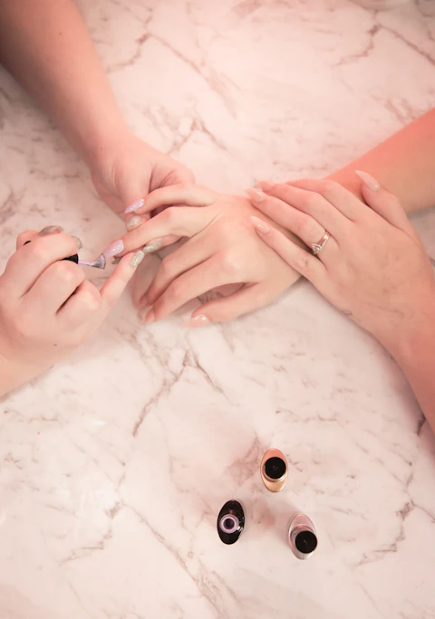 Manicurista trabajando sobre una mesa de mármol rosado junto a esmaltes